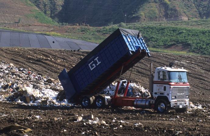 A dump truck dumping gravel on the side of a road.